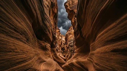 Dramatic view of a narrow slot canyon with towering sandstone walls under an ominous storm-filled sky