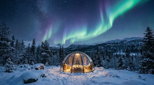 Transparent glass dome accommodation under the northern lights in arctic wilderness with snow-covered landscape